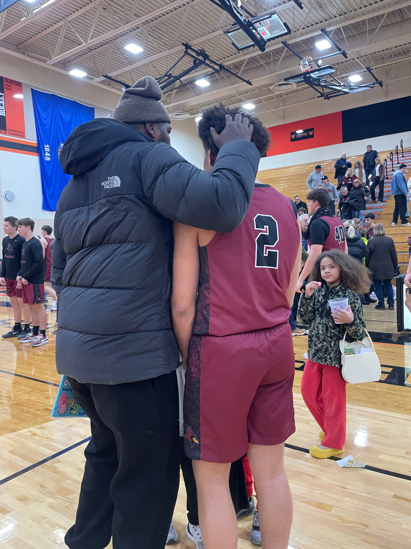 A mentor embraces a young athlete after a basketball game